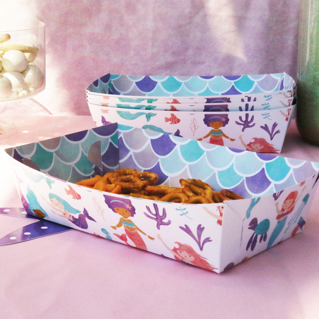 Colorful box with mermaid design containing snacks on a pink surface.