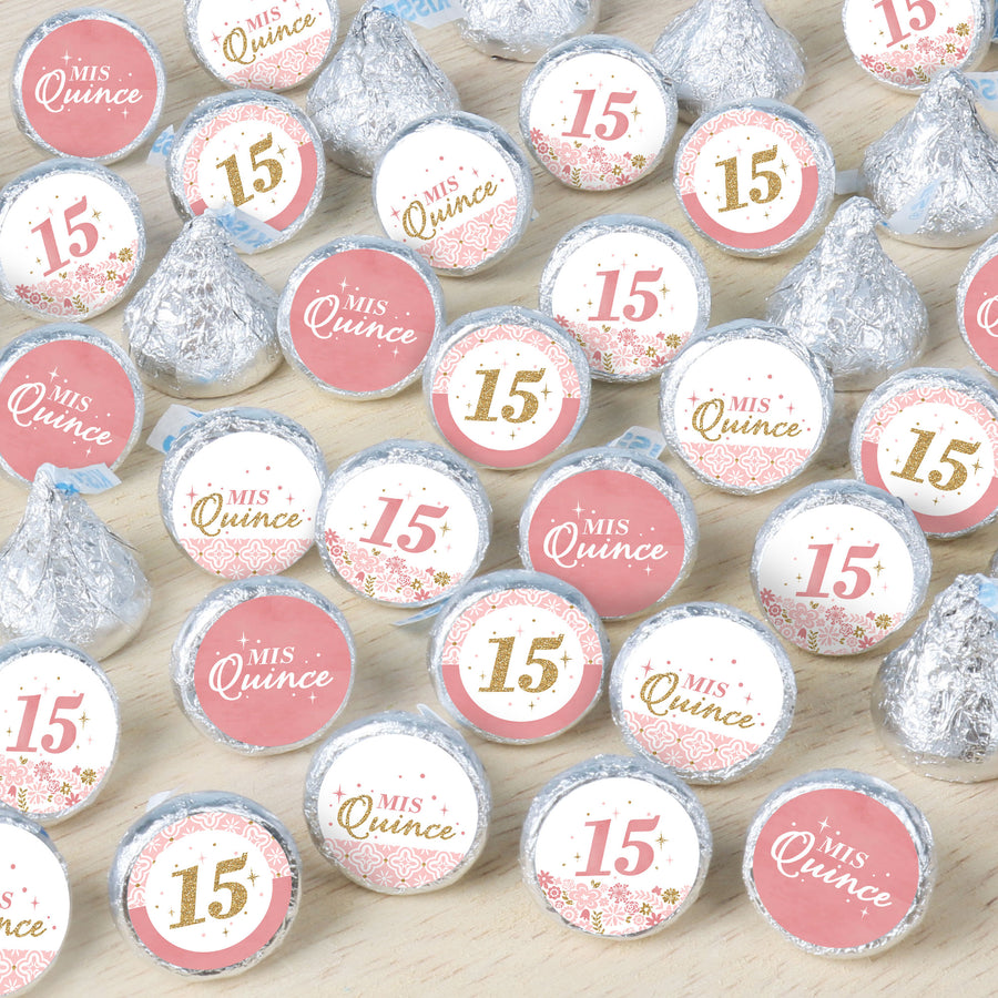 A collection of round candy stickers with 'Mis Quince Anos' and the number 15 printed in pink on a white background, displayed on a wooden surface.