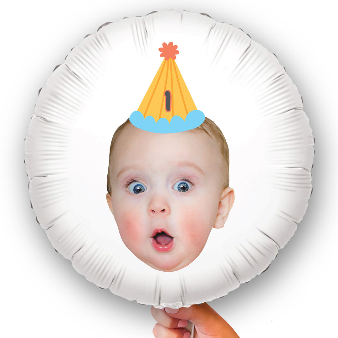 A round white balloon with a double-sided print including a photo of a surprised baby face wearing a birthday hat.