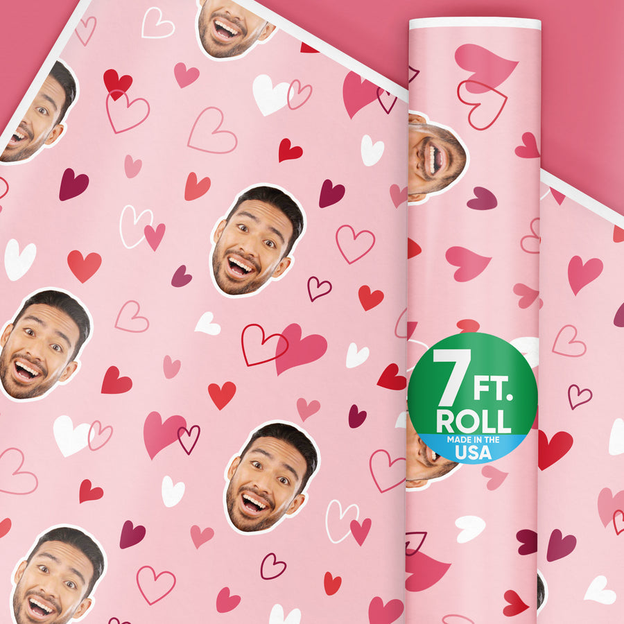 Customizable wrapping paper for Valentine's Day with a pink and red hearts pattern, featuring a smiling face, and a roll indicator stating 7 ft. Made in the USA.