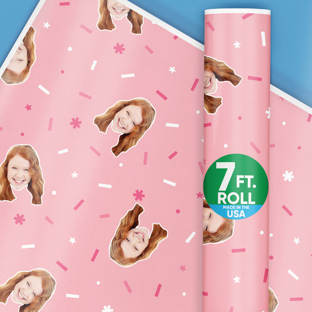 A roll of custom pink wrapping paper with a photo face design, and a badge indicating the paper is made in the USA.