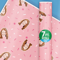 A roll of custom pink wrapping paper with a photo face design, and a badge indicating the paper is made in the USA.