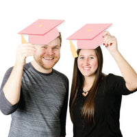 Two people holding pink graduation caps above their heads on a white background