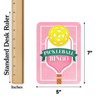 Party game Pickleball Bingo card with a yellow ball on a pink paddle, next to a ruler showing dimensions.