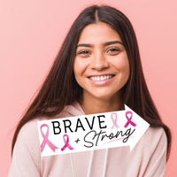 Woman wearing a pink hoodie with 'Brave + Strong' and pink ribbons on a pink background