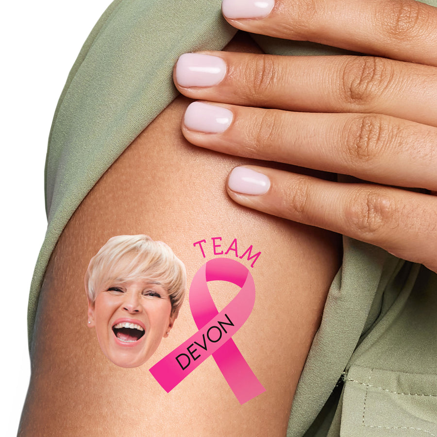 Person with a custom pink ribbon temporary tattoo on their arm, featuring a face and 'Team Devon' text.