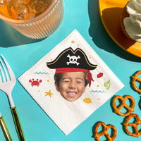 Custom Napkin with a pirate-themed design featuring a child's face, surrounded by snacks on a blue background.