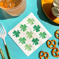 Napkin with green shamrock patterns on a blue tablecloth with food items.