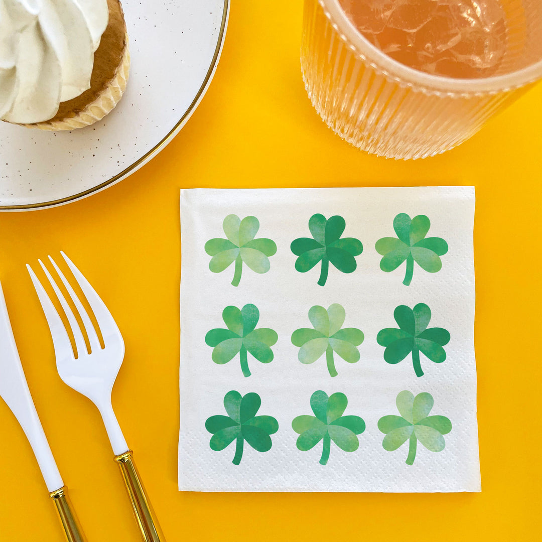 Napkin with green shamrock patterns on a yellow table with a fork and glass.