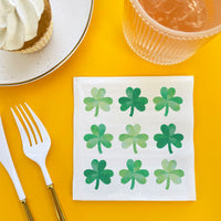 Napkin with green shamrock patterns on a yellow table with a fork and glass.