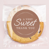 Cookie in clear packaging with a brown label saying 'A Very Sweet Thank You' on a light pink background