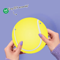 Yellow circular softball banner piece with white lines held by hands against a purple background, with 'bg' branding.