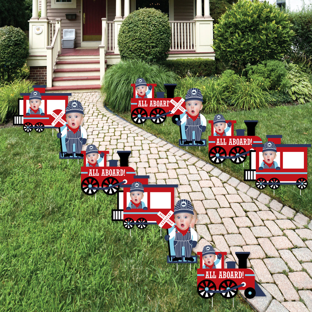 A set of 10 custom photo cut-out yard signs arranged in a train formation on a garden pathway, featuring a character in each sign.