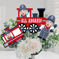 Custom photo centerpiece sticks with a red steam train design and cut-outs of children in conductor hats, set against a floral background.
