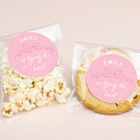 Popcorn and cookie packages with 'EMILY is tying the knot' labels on a beige background
