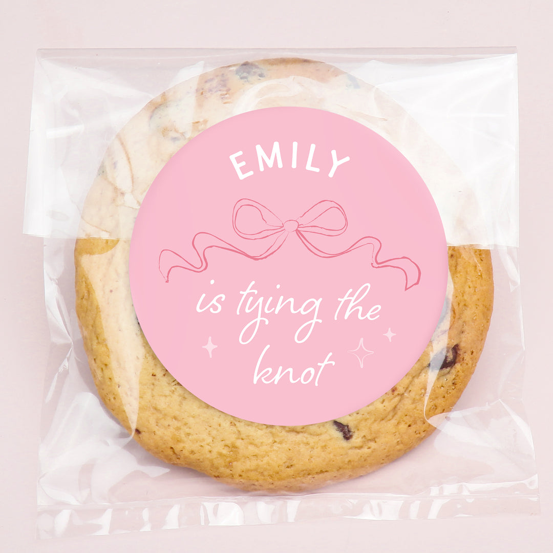 Cookie with a pink label reading 'EMILY is tying the knot' on a light pink background
