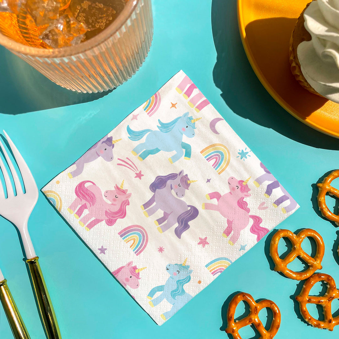 Unicorn-themed paper napkin on a colorful table with pretzels and cutlery.