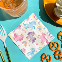 Unicorn-themed paper napkin on a colorful table with pretzels and cutlery.