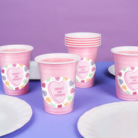 Pink personalized party cups with personalized labels on a purple background
