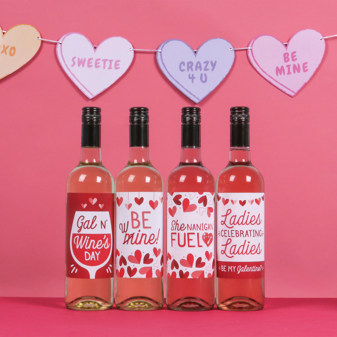 Four bottles of wine with decorative labels on a pink background with heart-shaped signs.