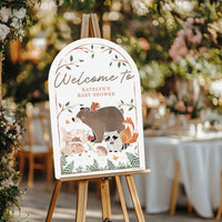 Baby shower welcome sign with animal illustrations on an easel, surrounded by floral decorations.