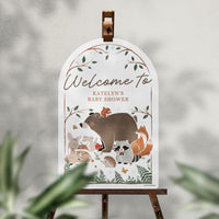 Woodland-themed baby shower welcome sign on an easel with a blurred natural background