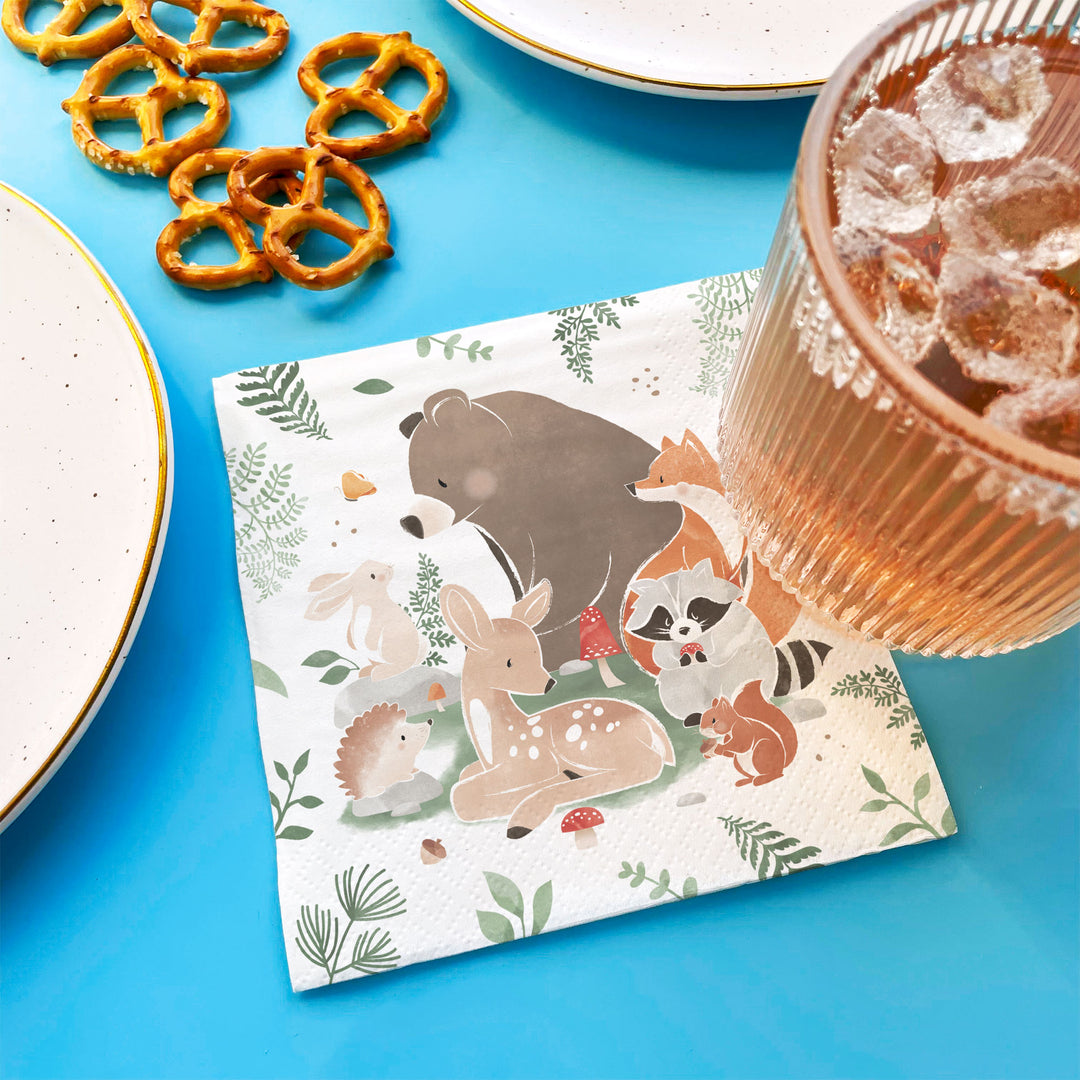 Napkin with forest animal design on a blue table with pretzels and a drink.