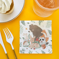 Napkin with forest animal design on a yellow table with cutlery and a cup.