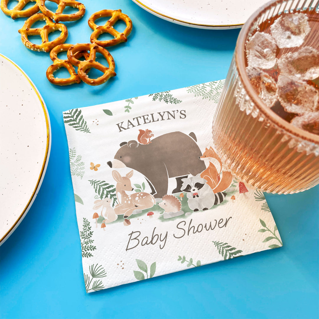 Custom Name Baby shower Napkin with animal illustrations on a blue surface with pretzels and a drink.