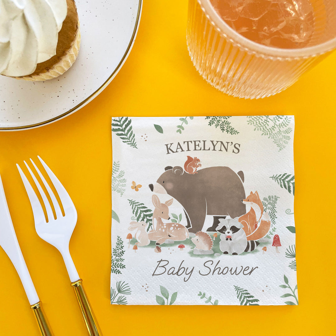 Custom Text Baby shower Napkin for dessert table with forest animals on a yellow tablecloth with cutlery and dessert.