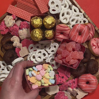 Galentine's day candy and treat boxes being places on a tray of desserts