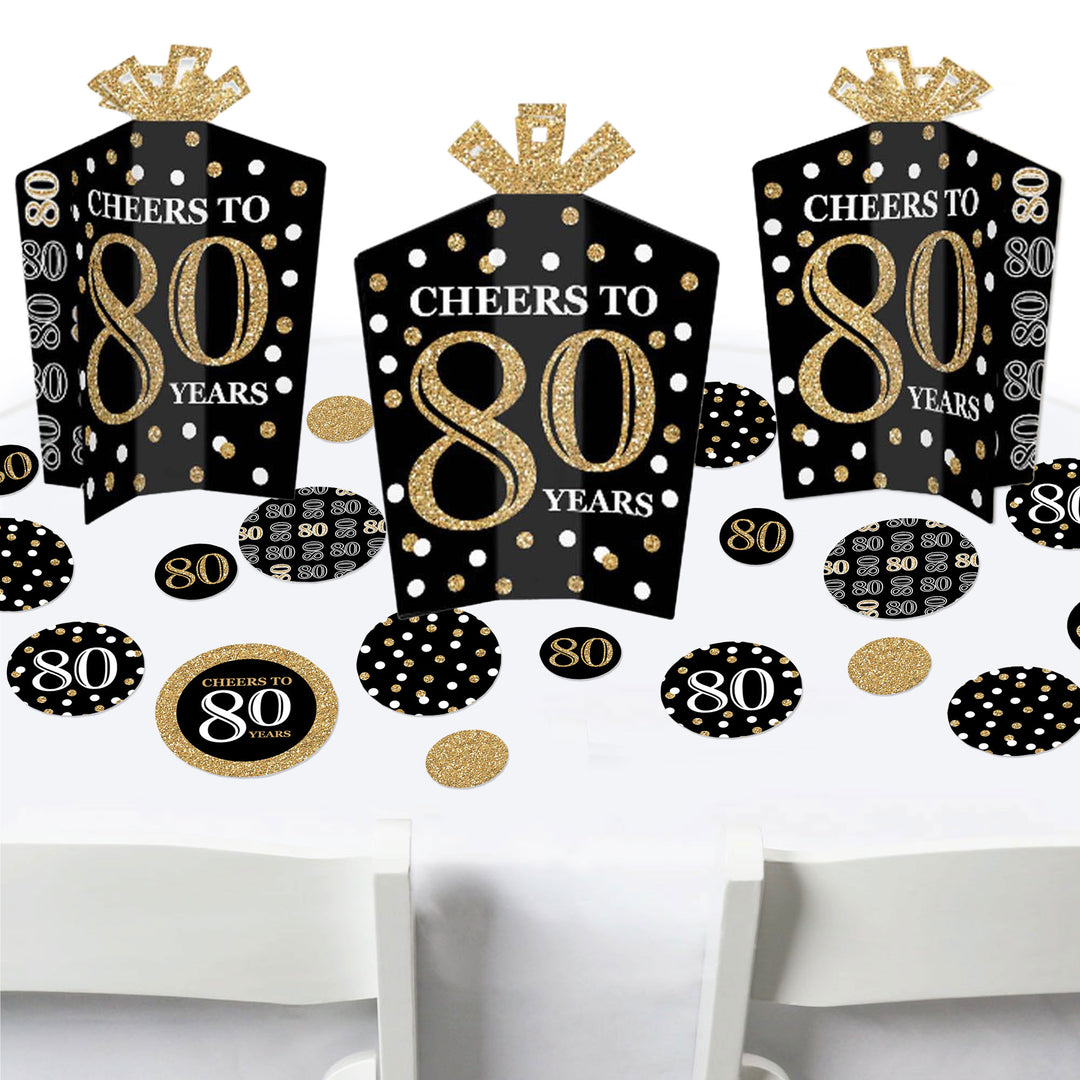 A set of adult 80th birthday party decorations in gold and black, including fold and flare table centerpieces and circular confetti.
