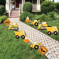 A set of construction-themed lawn decorations including yellow dump truck, bulldozer, and excavator figures, orange traffic cones, and construction sign decorations arranged on a garden path.