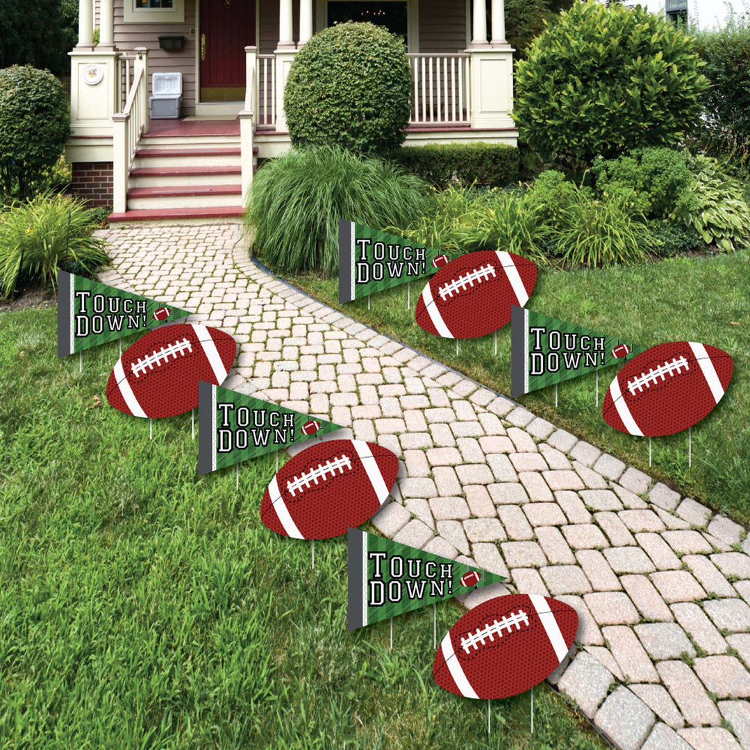 A set of football-themed lawn decorations displayed on a garden path, consisting of yard signs with the text 'Touch Down' and images of footballs.