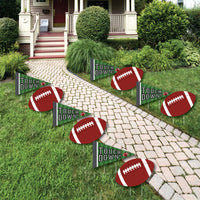 A set of football-themed lawn decorations displayed on a garden path, consisting of yard signs with the text 'Touch Down' and images of footballs.