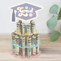A Groovy Grad Cash Cake stand with rolled-up bills placed in it, designed to resemble a two-tier cake with a graduation cap motif.