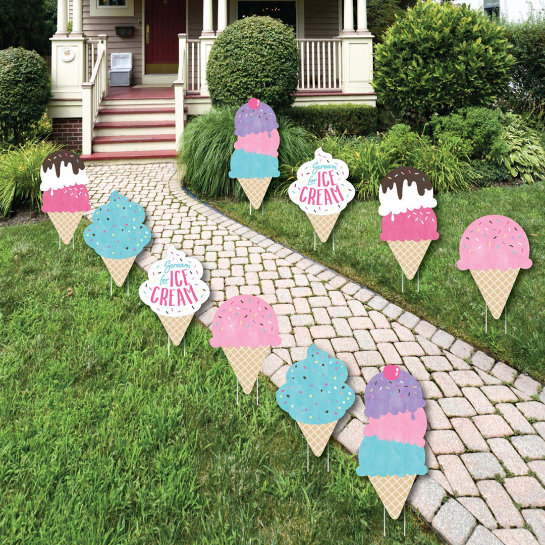 A set of colorful 'Scoop Up The Fun - Ice Cream' lawn decorations displayed on a grassy area in front of a house, consisting of various ice cream cone shapes with sprinkles and the text 'ICE CREAM'.