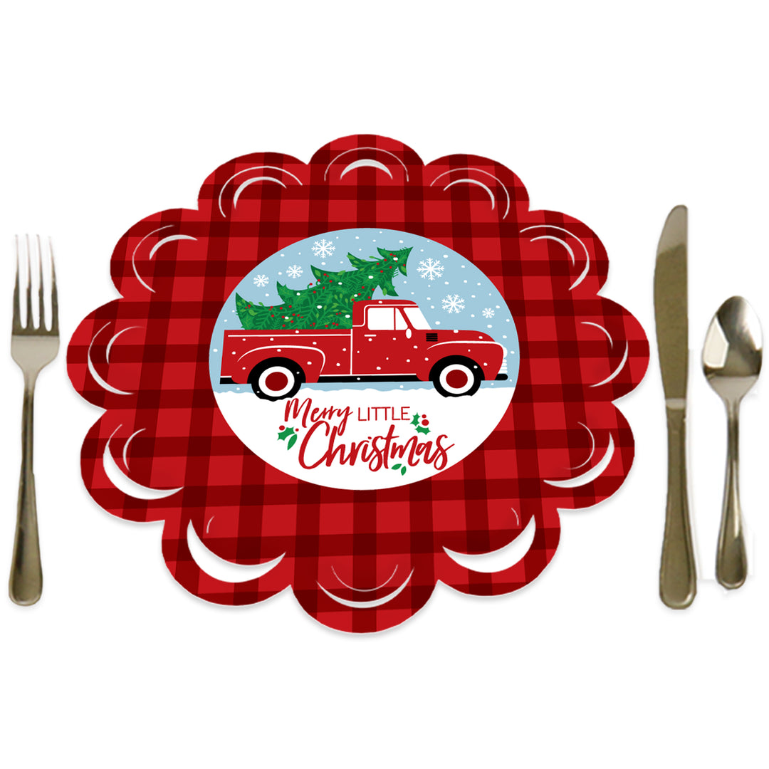 A round red paper charger with a scalloped edge featuring a Christmas tree and a red truck in the center, surrounded by a fork, knife, and spoon on a white background.