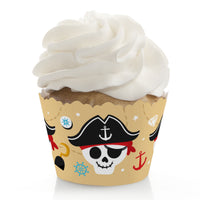A cupcake with a beige wrapper featuring pirate-themed decorations, including a skull, pirate hat, and ship wheels, topped with a swirl of white frosting.
