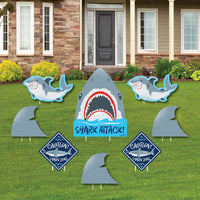 A set of shark-themed yard signs displayed on a lawn, featuring a large shark head, smaller shark shapes, and 'CAUTION' signs with shark fins.