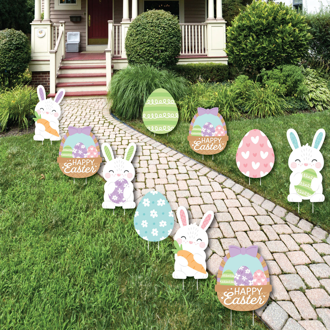A set of Easter-themed lawn decorations displayed on a garden path, featuring cut-outs of bunnies, eggs, and baskets with 'Happy Easter' messages.
