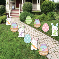 A set of Easter-themed lawn decorations displayed on a garden path, featuring cut-outs of bunnies, eggs, and baskets with 'Happy Easter' messages.