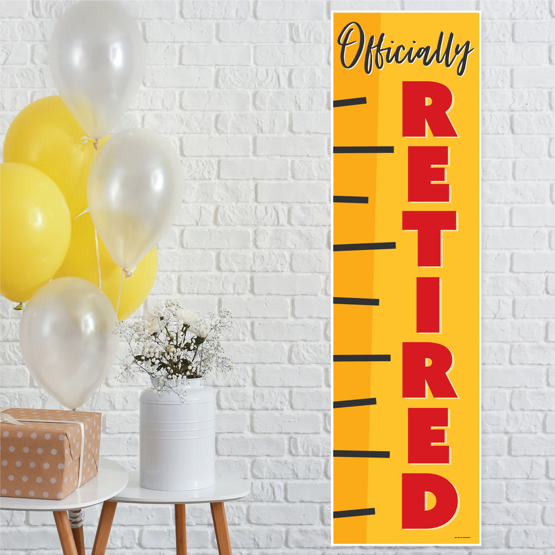 A vertical banner with the text 'Officially Retired' in bold red letters on a yellow background, displayed at a party with balloons and decorations.