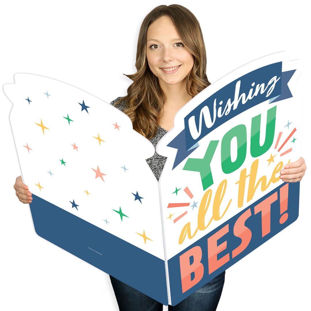 A person holding a large, colorful greeting card that reads 'Wishing You All The Best!' decorated with multi-colored stars.