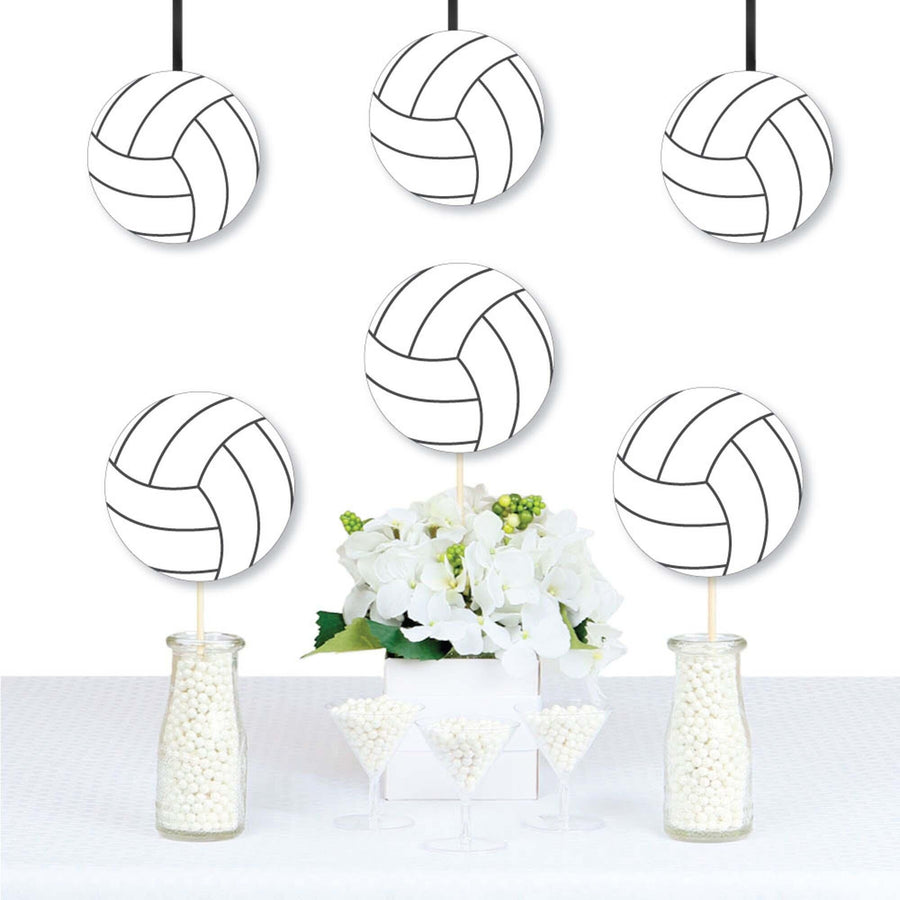 A set of volleyball-shaped decorations printed in black and white, displayed hanging from strings above a table decorated with flowers.