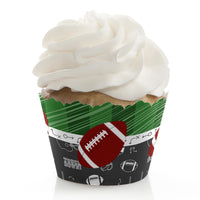 A cupcake with a white frosted top wearing a wrapper with football-themed patterns for a baby shower decoration.