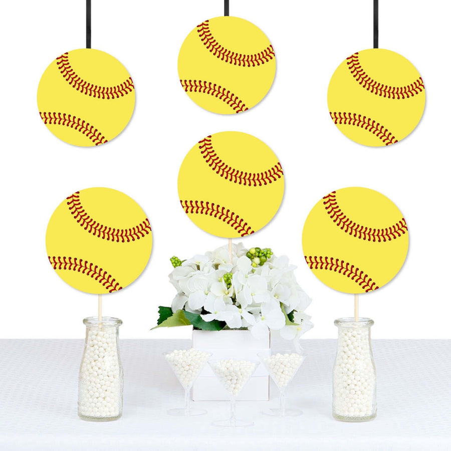 A set of yellow softball-shaped decorations with red stitching are displayed hanging from strings, arranged in front of a white floral arrangement, presumably part of a party decoration set.