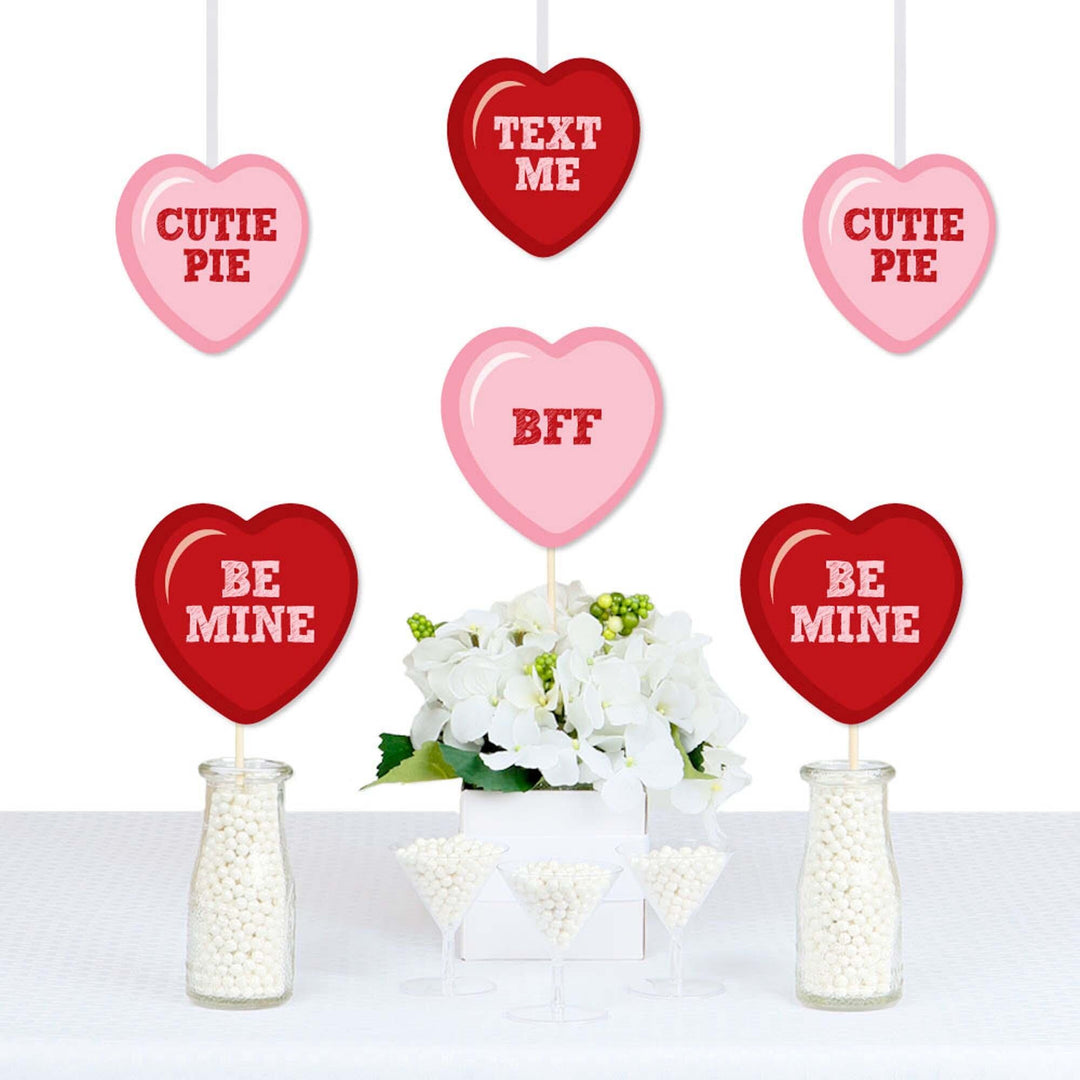 A set of heart-shaped decorations for Valentine's Day, with various messages printed on them, displayed in front of a floral arrangement.