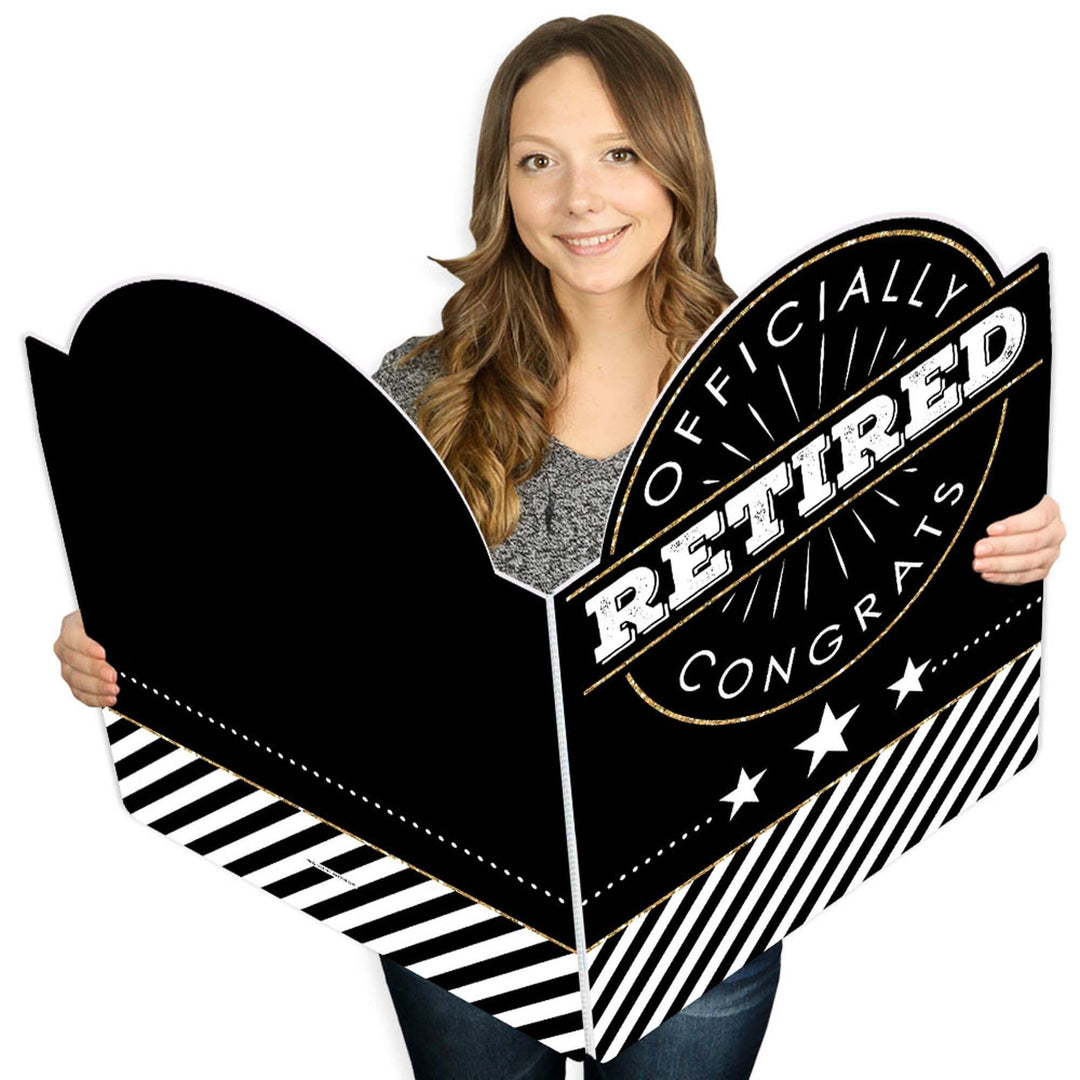 A person holding a large, black and white, congratulations greeting card that reads 'OFFICIALLY RETIRED' in bold letters.