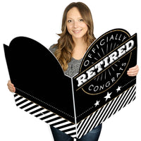 A person holding a large, black and white, congratulations greeting card that reads 'OFFICIALLY RETIRED' in bold letters.